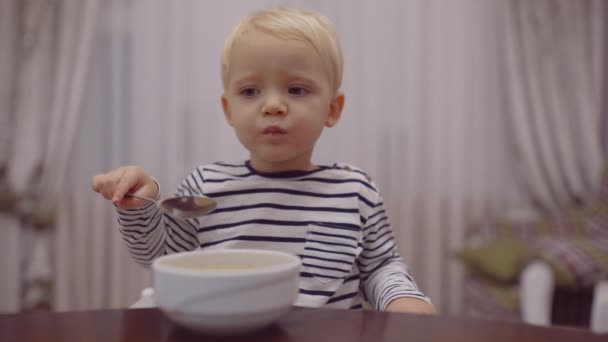 Bambino allegro mangia il cibo stesso con cucchiaio. Sorridente felice adorabile bambino mangiare purè di frutta in cucina. Ragazzo carino stanno mangiando . — Video Stock