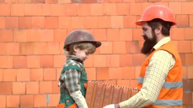 Tuğla ya da taş bloklardan duvar ören küçük bir evlat. Oğul yardımcı. Hard Hat 'ta inşaat bloklarında ailesiyle oynayan bir çocuk. Küçük oğlu inşaatta babasına yardım ediyor..