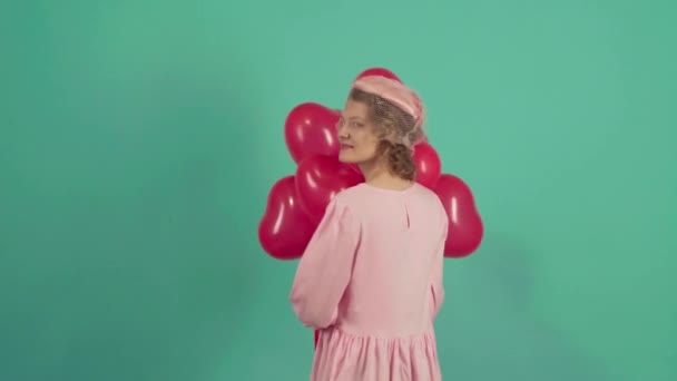Радісна модель, що подає, розважається, святкує День святого Валентина. Валентина Красуня з червоними повітряними кулями сміється на зеленому тлі. Чудова молода жінка. Святкове свято. — стокове відео