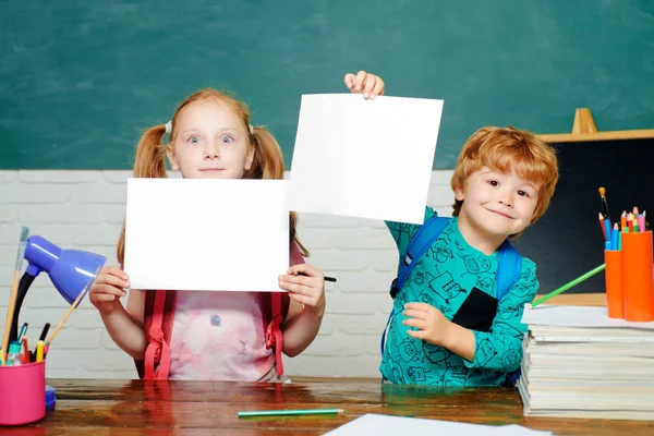 De volta à escola. Crianças pequenas engraçadas apontando para cima no quadro-negro conceito da escola. Educação. Espaço de cópia de papel . — Fotografia de Stock