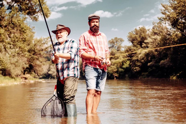 Gelukkige vader en zoon samen vissen in de zomerdag onder prachtige hemel op de rivier. Visser en trofee forel. Nog water forel vissen. — Stockfoto