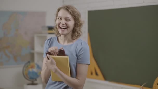 Lehrerin im Unterricht vor dem Hintergrund der Tafel. Studentin oder Lehrerin mit Büchern im Klassenzimmer. — Stockvideo