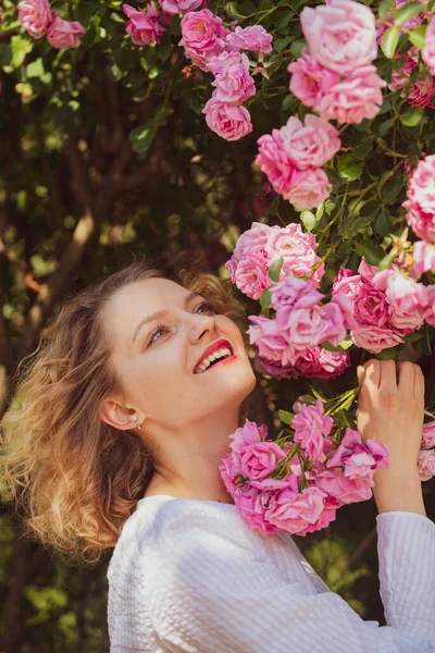 Hermosa mujer sostiene la floración rosa rosal. Concepto Rose. Florecen alrededor. Hermosa mujer con flores de rosa bastante florecientes. Mujer feliz caminando en el jardín de rosas . — Foto de Stock