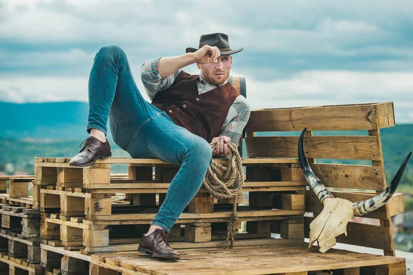 Nyugati élet. Borotválatlan fickó cowboy kalapban és fonott ingben, messzire néz. Jóképű szakállas macsó. Férfi szépségápolási előírás. Példa az igazi férfiasságra. Cowboy kalapban.. — Stock Fotó