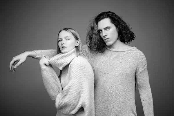 Stylish confident male and female models with nature hairstyle wearing a yellow and green sweater and standing close together looking alluringly at camera.