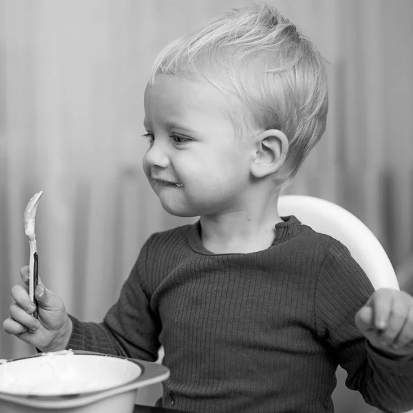 Çocuk sevimli bebek kahvaltı yiyor. Bebek beslenmesi. Sağlıklı yiyin. Toddler evde atıştırmalık yiyor. Çocuk lapa yer. Çocuk sevimli çocuk mavi gözleri tabak ve gıda ile masada oturup. Sağlıklı beslenme. Sağlıklı gıda — Stok fotoğraf