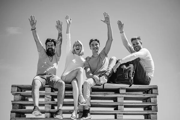 明るい友人のグループは、ベンチに座って青い夏の背景で手を上げています。人とのコミュニケーションと友情の概念. — ストック写真