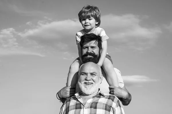 Fête des pères - grand-père, père et fils s'embrassent et s'amusent ensemble. Enfant heureux jouant sur fond de ciel d'été . — Photo