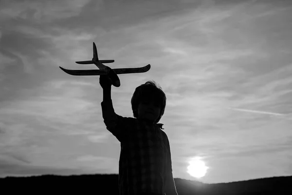 Rapaz aviador ao pôr-do-sol. Crianças pequenas com avião de brinquedo em um campo ao pôr do sol. Sucesso e conceito de líder infantil. — Fotografia de Stock