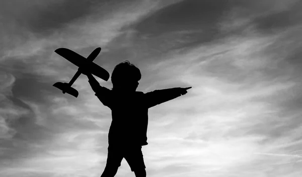 Black silhouette of cute happy child running at countryside and holding toy plane in hand. Cute child playing with toy airplane in the meadow in vintage color tone. Childhood concept.