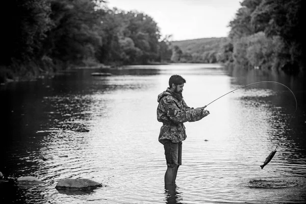 Άνδρας που χαλαρώνει και ψαρεύει δίπλα στη λίμνη. Αλιευτικός εξοπλισμός ψαράδων. Σ / Κ. Επιτυχημένο πιάσιμο. Χαρούμενος μουσάτος ψαράς στο νερό. Άντρας με καλάμι ψαρέματος. Πιάσιμο ψαριών. — Φωτογραφία Αρχείου