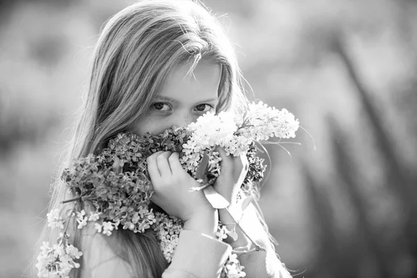 Una niña guapa y de moda en el jardín con el pelo largo y rubio emocionada de conseguir un ramo de lila en un cumpleaños . — Foto de Stock