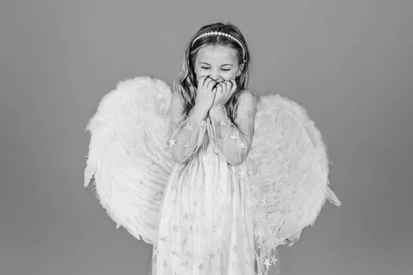 バレンタインデー。天使のように見えるブロンドの巻き毛の天使の子供白いドレスのかわいい子供の女の子が色の背景の上に立っている。天使の翼を持つ美しい天使の女の子の肖像. — ストック写真