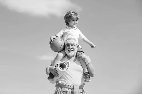 Abuelo y nieto con pelota de baloncesto y esterilla de yoga en las manos. Padre e hijo haciendo ejercicio. La edad no es excusa para aflojar tu salud. . —  Fotos de Stock