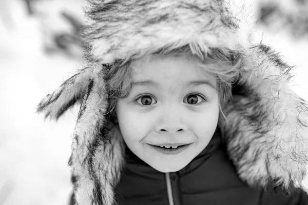 Winter kid excited face close up. Happy winter time. Happy child playing with snow on a snowy winter walk.
