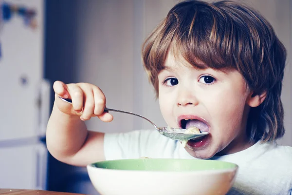 Hongerig jongetje aan het eten. Vrolijk baby kind eet voedsel zelf met lepel. Lekkere kinderen ontbijten. Baby eet eten in de keuken. Happy baby jongen eet gezond voedsel lepel zelf. — Stockfoto