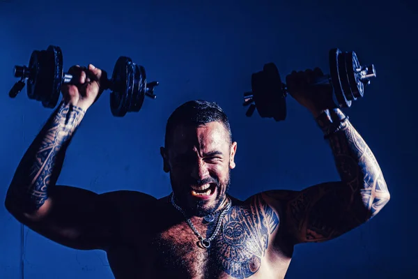 Ung muskulös bodybuilder Guy gör övningar med hantlar över mörk bakgrund. Intensivt träningspass. — Stockfoto