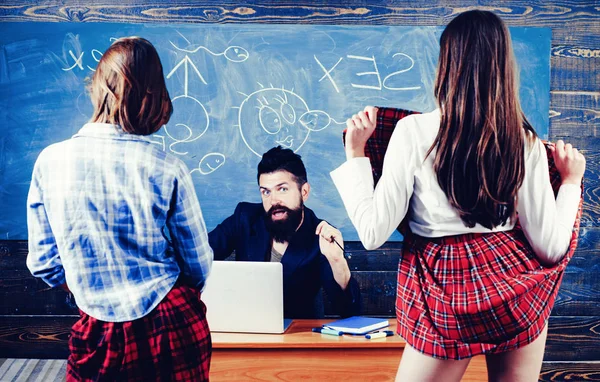 Bearded sexology teacher looks at two sexy female students. Erotic education and sex Symbols on chalkboard. Anatomy lesson and sex education in high school. — Stock Photo, Image