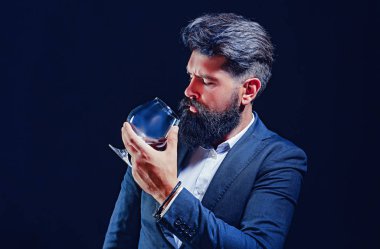 Confident bearded man in black suit with glass of whisky in loft. Confident well-dressed man with glass of whisky.