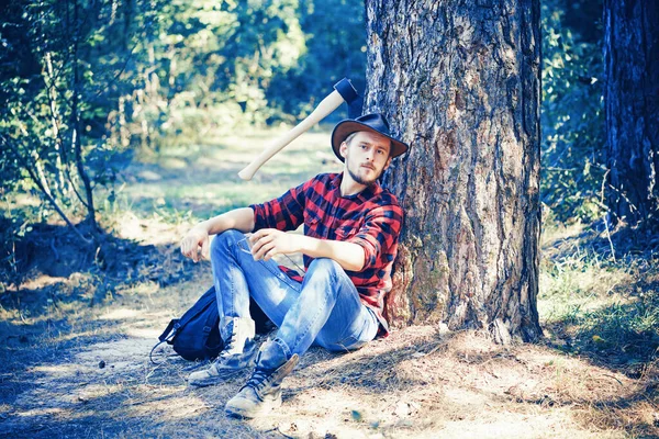 El leñador trabajando en un bosque. Hermosa Woodworkers leñador camisa a cuadros sosteniendo el hacha en el fondo de la naturaleza verde. Un joven guapo con barba lleva un árbol . —  Fotos de Stock