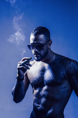 Pahalı tütün. Puro sigara yaşam an tadını çıkarın. Sakallı kas maço güzel gövde moda güneş gözlüğü sigara puro. Elit tütün. Saf zevk. Tütün tüketmek. Puro ile Dövmeli adam