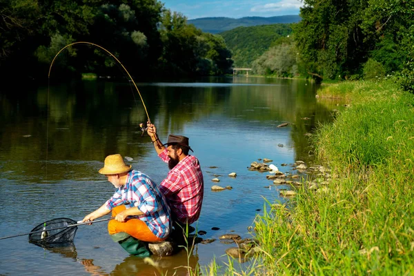 Happy fishermen friendship. Fishing. Bearded fisher in water. Giving your hobby. Real happiness. Summer weekends or vacation. Fish normally caught in wild. Fishers have long rods. Rest and recreation. — Stockfoto