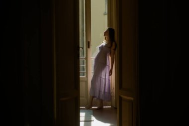 Balkonun yanında duran genç bir kadın. O mutlu dans eder. Kız gece kıyafeti giymiş. Tatil ve tatil. Seksi iç çamaşırlarıyla mükemmel bir kadın vücudu. Kadın modası..