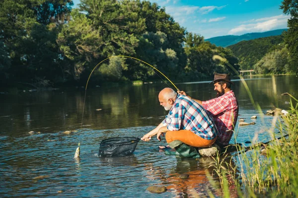 Homme mature avec fils adulte pêche. Un passe-temps masculin de pêcheur. Pêche à la mouche réussie. Joyeux pêcheur mature pêche dans une rivière en plein air . — Photo