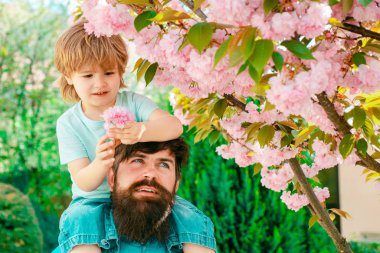 Cute boy sitting on fathers shoulders. Father giving son ride on back in park. Happy childhood concept. Fathers day.