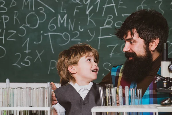 Teacher and kid. Teacher teaches a student to use a microscope. Elementary school kid and teacher in classroom at school. Daddy and son together — Stok fotoğraf