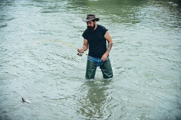 Homem a pescar no rio. Férias. Atividades desportivas de passatempo. Um tipo de chapéu. Peixe no anzol. Peixes normalmente capturados em estado selvagem. Pothunter. Belo dia para pescar. Homem de idade pesca . — Fotografia de Stock