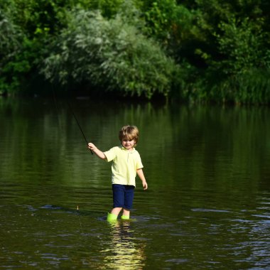 Young boy standing in river with fishing rod on sunny day. Cute boy is fishing in the river in the summer. Cute little boy fishing on pond.