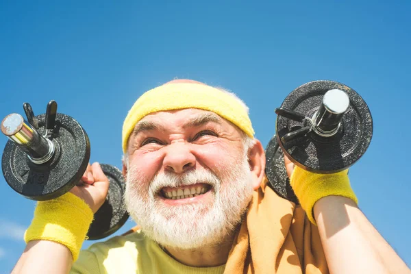 Age is no excuse to slack on your health. Senior man exercising on blue sky. Health club or rehabilitation center for elderly aged pensioner. Senior sport man lifting dumbbells in sport center. — 스톡 사진