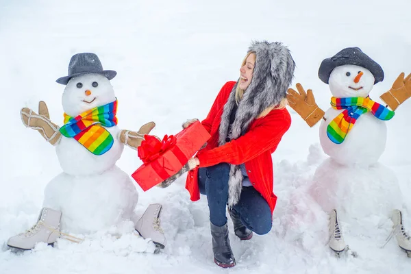 Téli waman hóemberrel a háttérben. Téli portré egy szépséglányról a Hókertben. Aranyos hóember téli lány áll télen karácsonyi táj. — Stock Fotó