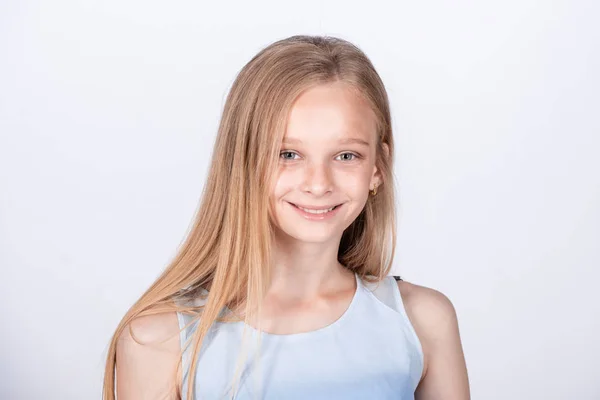 Cute European little girl waiting for mom to pick her up after dance classes. A beautiful female child with blonde hair in a blue t-shirt, standing casually over white background, being calm. — Stock Photo, Image