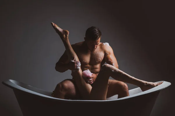 Beautiful female legs relaxing in white bath. Family couple of man and sexy girl. Couple in love. Woman legs in bath foam. Total relaxation. Muscular man. Guy sitting in bath tub. — Stok fotoğraf