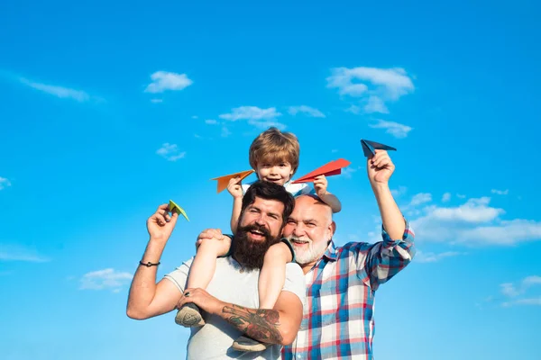 Piloto de niño con jetpack de juguete contra el fondo del cielo. Feliz tres generaciones de hombres se divierten y sonríen en el fondo del cielo azul. Niño feliz jugando al aire libre . — Foto de Stock