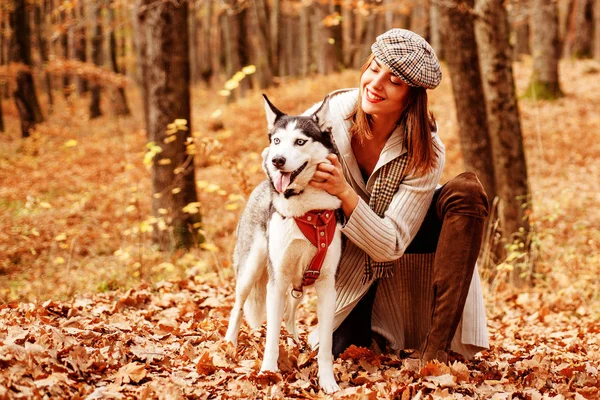 Good looking stylish girl is playing with her husky dog in the autumn forest. Fall is the best time of the year to have a walk with your pet. Autumnal nature and walk with pet concept. — Stock Photo, Image