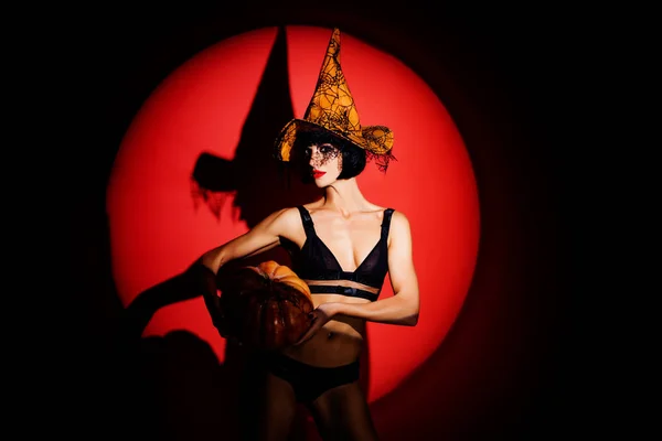 Halloween sexy concept. Erotic girl in black lingerie with a witch hat. Holding the yellow pumpkin. Halloween party for adults. — ストック写真