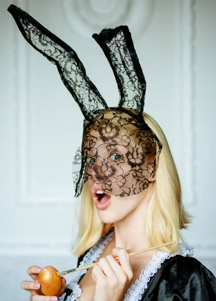 Attractive young woman wearing bunny ears and holding up a colorful Easter egg. Sexy blonde girl with lace bunny ears. Woman easter.