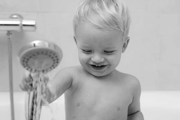 Piccolo e curioso bambino seduto nel bagno bianco con i capelli bagnati in schiuma che distolgono lo sguardo. Bambino adorabile sotto un asciugamano incappucciato dopo il bagno . — Foto Stock