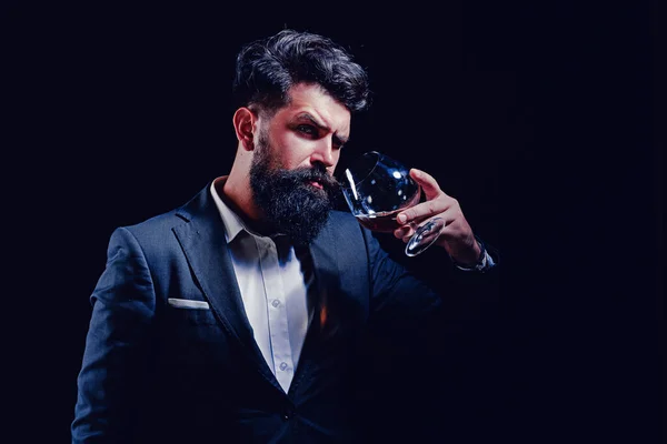 Conceito de álcool. Homem barbudo elegante elegante Bartender detém vidro conhaque. Homem ou homem de negócios bebe conhaque em fundo preto. — Fotografia de Stock