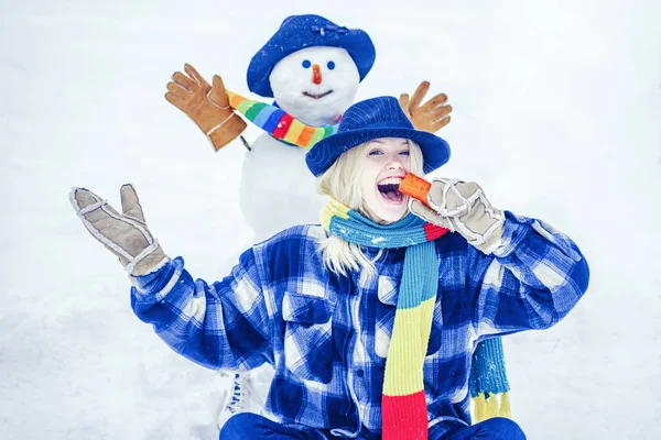 Snö man med rolig morotsnäsa. Snögubbe och rolig kvinnlig modell står i vinter hatt och halsduk med röd näsa. — Stockfoto