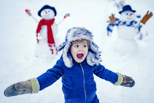 Vinterporträtt av ett litet pojkbarn i snön Trädgården gör snögubbe. Barn leker med Snowman på snö bakgrund. Vinterbarn i frostig vinterpark. — Stockfoto