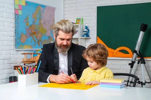 Father teaching son. Funny little child with father having fun on blackboard background. Supporting pupils at school. Private kids tutoring.