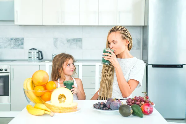 Mulher feliz mãe e menina filha bebe smoothie verde na cozinha. Mãe e filha com copo de smoothie desintoxicação natural na cozinha. Suplementos alimentares . — Fotografia de Stock