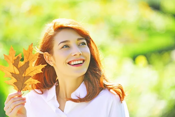 Happy smiling girl with natural red hair. Autumn woman with bright orange hair. Cheerful smiling ginger woman holding fall oak leaves. Healthy and natural woman beauty. — ストック写真