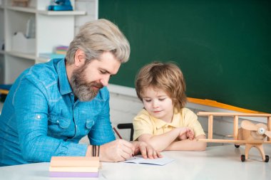Cute little preschool kid boy with teacher study in a classroom. Young happy family father and son schooling math together. School kids.