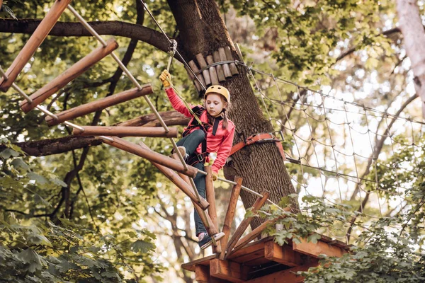 Chaque enfance compte. Joyeux enfant en été. Petit garçon profiter des années d'enfance. Enfant grimpant sur un parc à cordes. Randonnée dans le parc à cordes fille en équipement de sécurité . — Photo