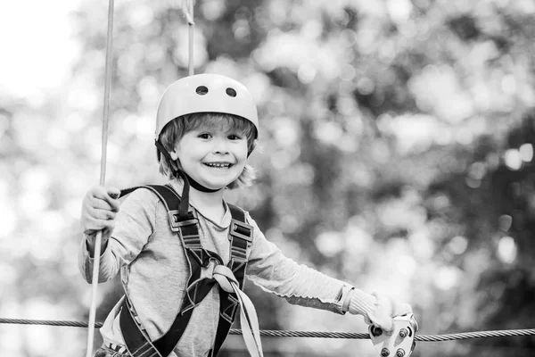 Children summer activities. Adventure climbing high wire park. Cute baby boy playing. Hiking in the rope park girl in safety equipment. Happy child climbing in the trees. Child.